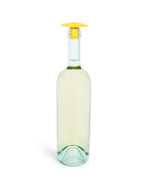 A clear glass wine bottle with a pale yellow liquid inside and a bright yellow silicone Whine Stopper, isolated on a white background.