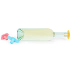 A clear glass wine bottle filled with pale yellow liquid, shown horizontally on a white background with two Whine Stoppers in red and blue, plus a yellow lion Whine Stopper on the bottle's end.