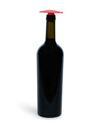 A dark glass wine bottle with a black neck and a bright red silicone Whine Stopper, shown against a plain white background.
