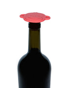 A red silicone wine bottle stopper with a monkey face design, shown on the neck of a dark glass wine bottle against a white background. This is also a children's teether made of food-grade silicone