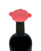A bright red monkey-shaped silicone bottle stopper and teether resting on the neck of a dark glass wine bottle, isolated on a white background.
