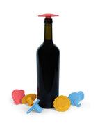 A dark glass wine bottle with a Whine Stopper standing upright, surrounded by five colorful animal-shaped Whine Stoppers in red, yellow, and blue on a white background.