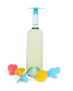 A clear glass wine bottle with a light blue Whine Stopper and five colorful child-friendly Whine Stoppers in red, yellow, and blue, arranged on a white background.